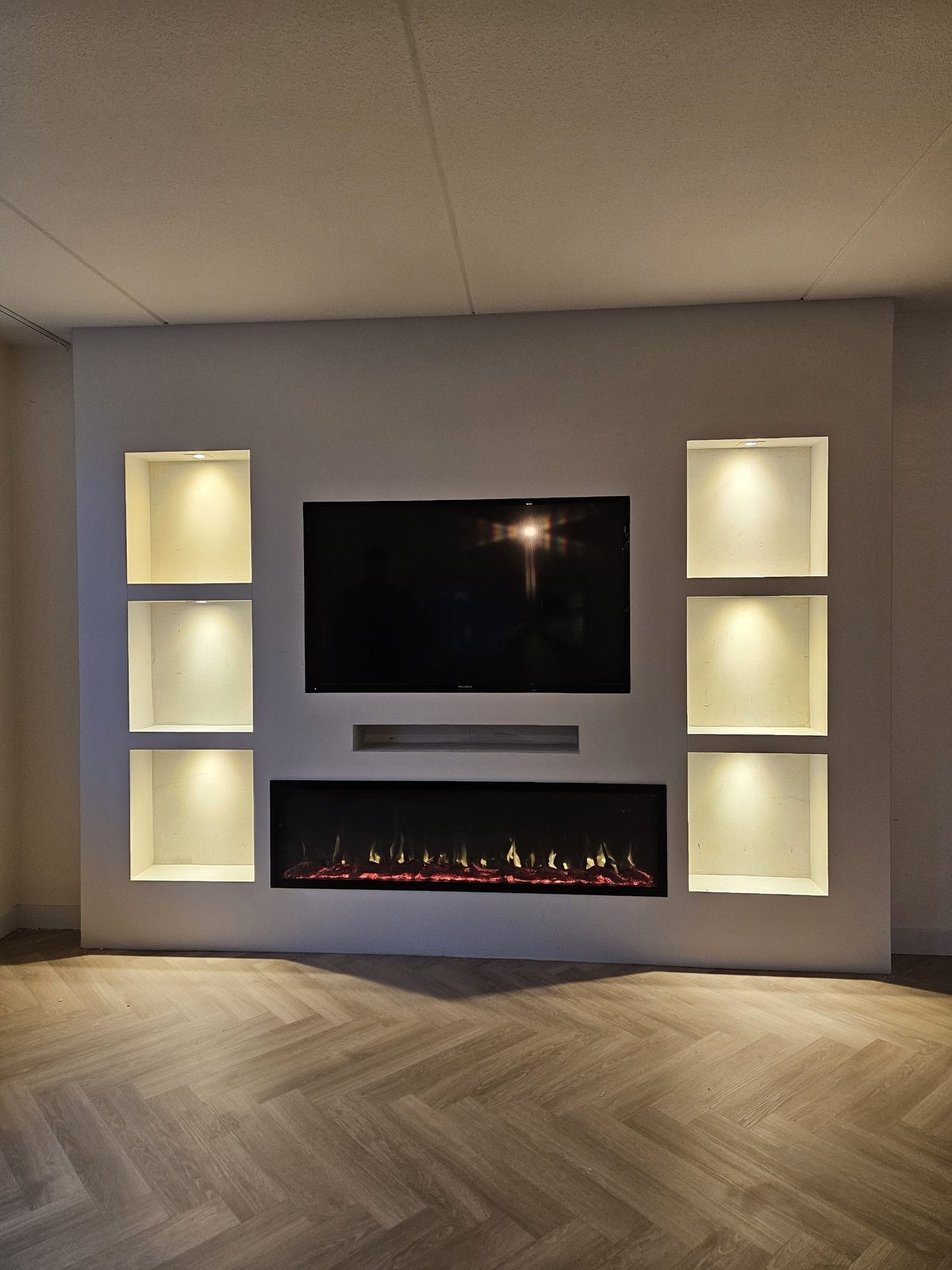 Witte cinewall met sfeerhaard en verlichte nissen in Almere 2 Afgewerkte witte cinewall in Almere met sfeerhaard, soundbarnis en zes verlichte nissen