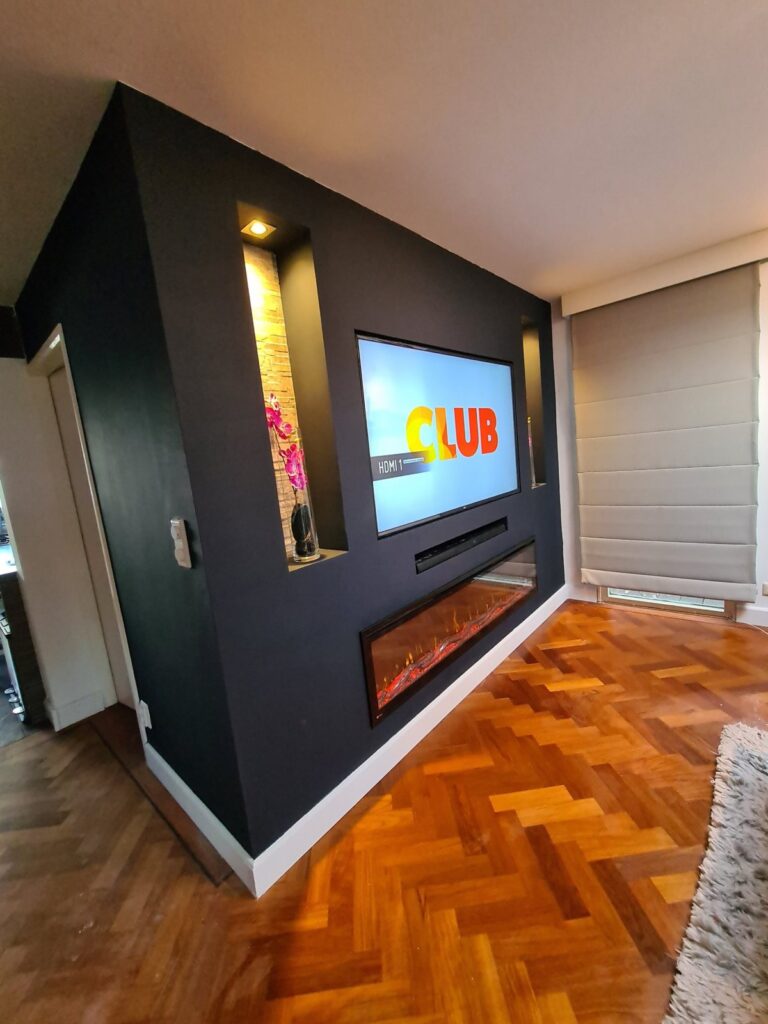 Donkere cinewall met sfeerhaard en verlichte nissen in Vlissingen 4 Verlichte nis met steenstrips en inbouwspot naast de tv in Vlissingen