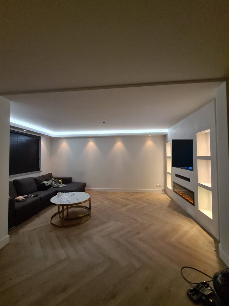 Cinewall met sfeerhaard, verlichte nissen en led-koof in Emmen 2 Woonkamer in Emmen met cinewall, sfeerhaard en verlichte nissen onder een led-koof