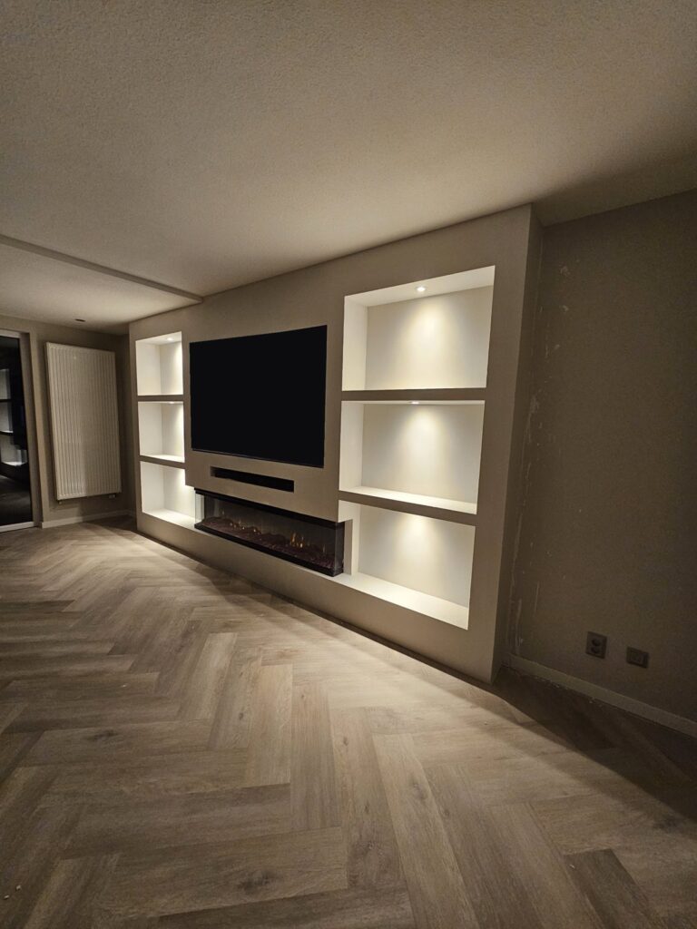 Brede cinewall met driezijdige sfeerhaard en verlichte nissen in Heerlen 2 Schuin aanzicht van de cinewall met driezijdige sfeerhaard in Heerlen