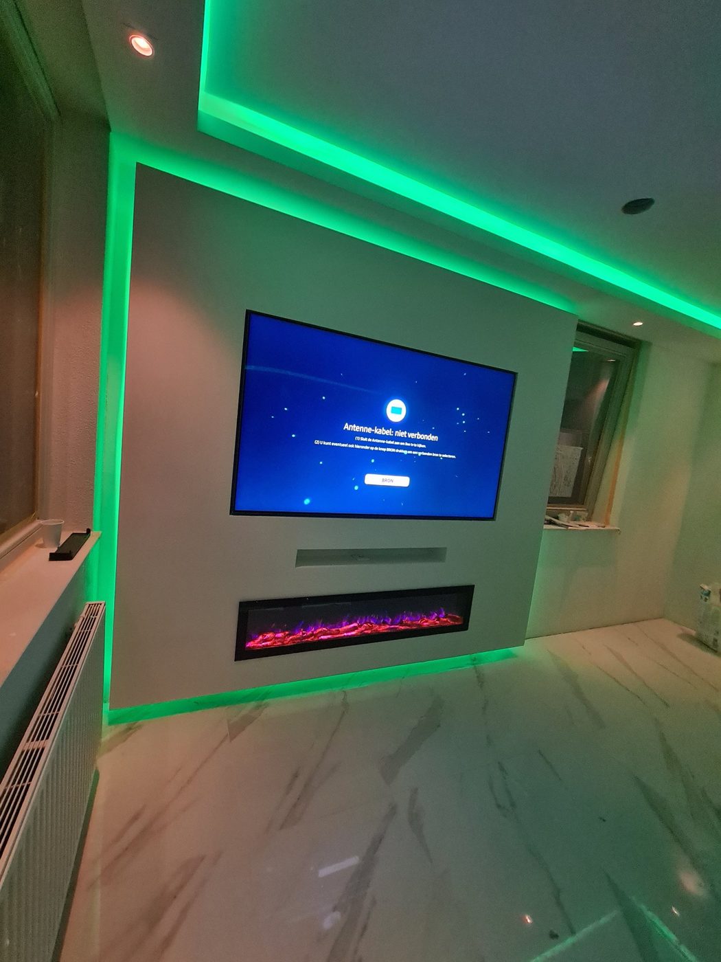 Koof met groene LED-verlichting rond een tv-wand met sfeerhaard