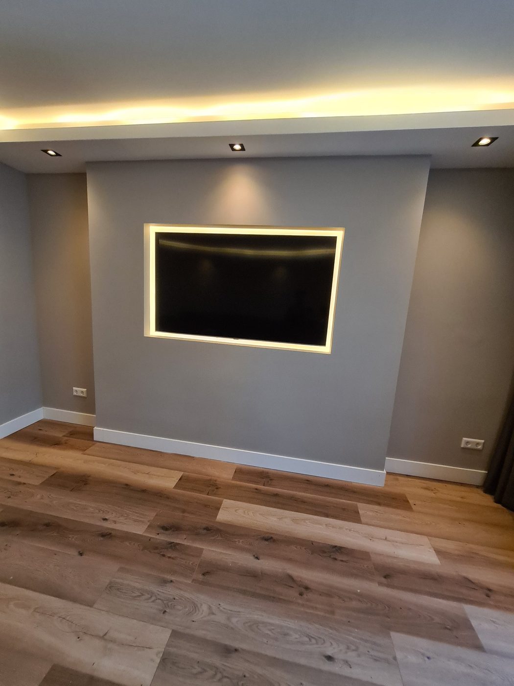 Koof met LED-verlichting en spots boven een tv-wand met verlichte rand