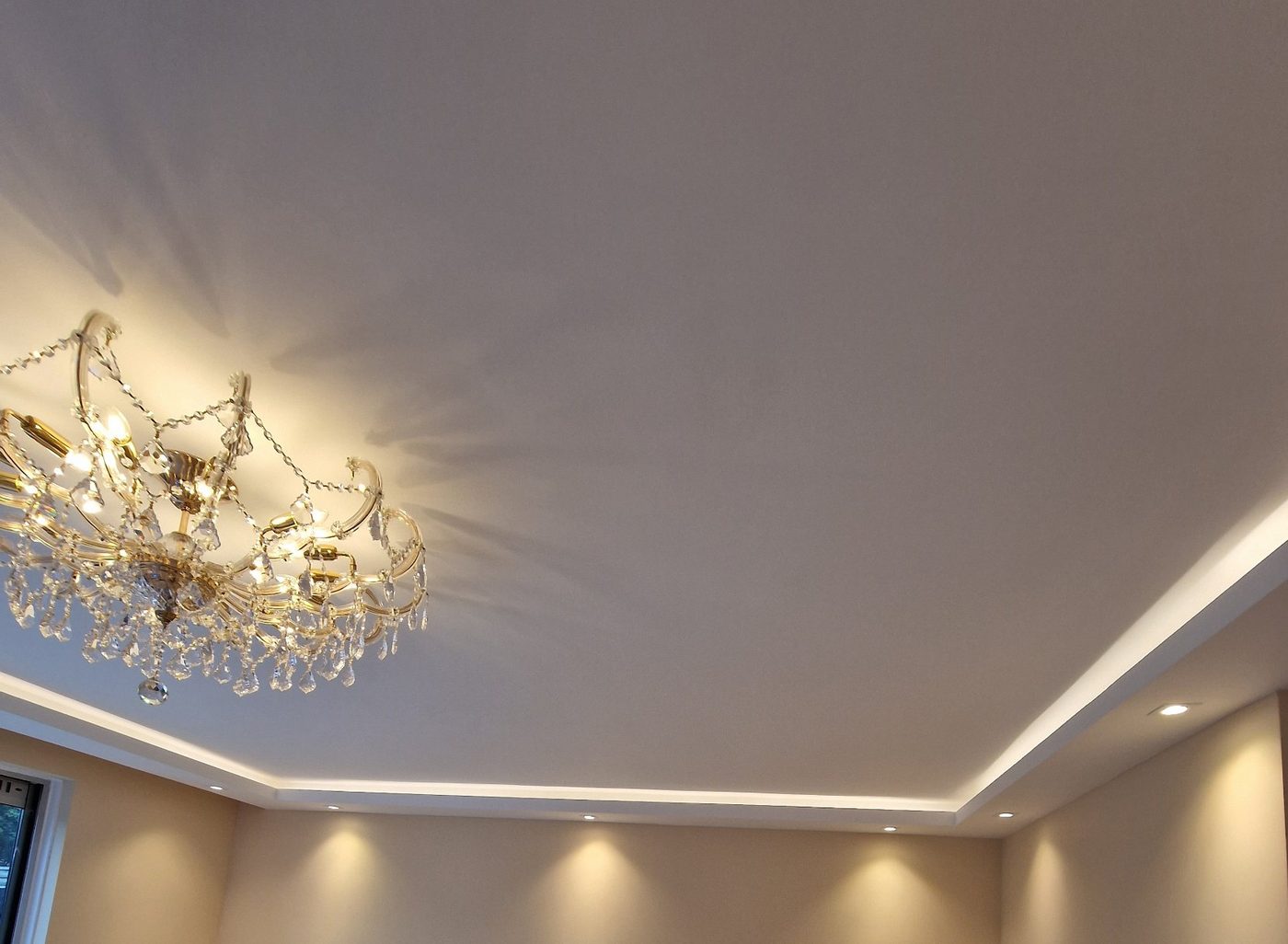 Koof met LED-verlichting en spots rond een woonkamerplafond met kroonluchter