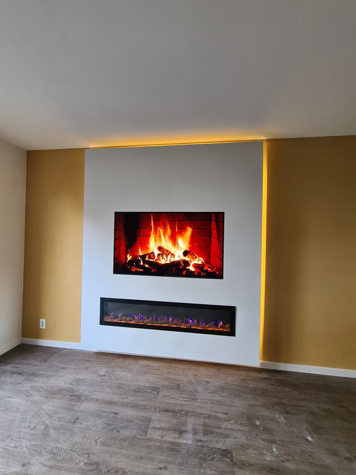 Witte cinewall met tv-nis, extra brede elektrische sfeerhaard en indirecte led-verlichting in Naaldwijk